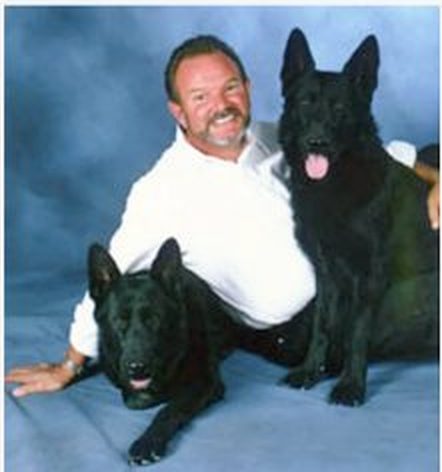Bob Taylor seated with two black German Shepherds